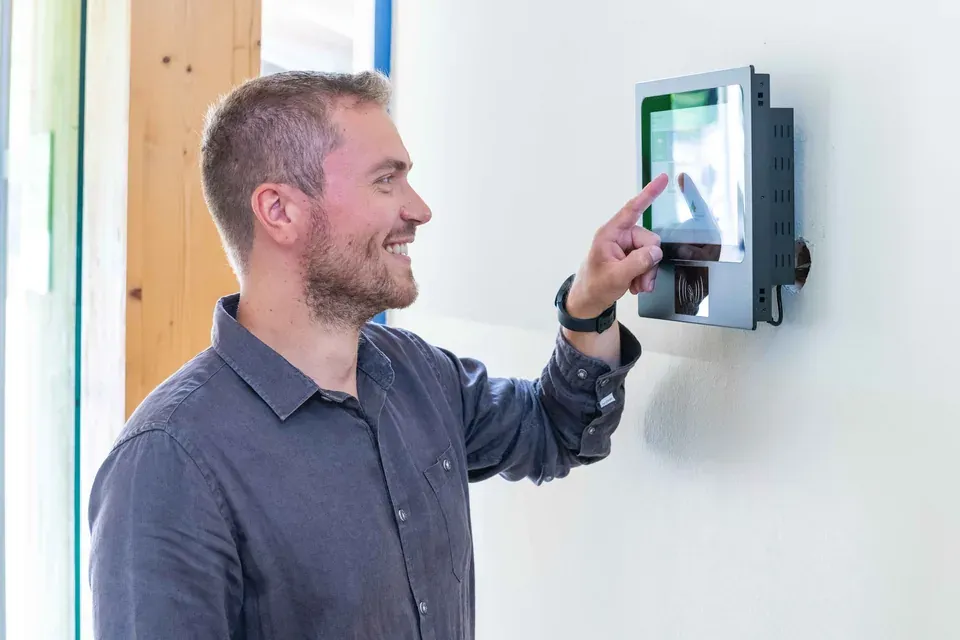 Mitarbeiter stempelt lächelnd am Timework Wand-Terminal mit Touchscreen